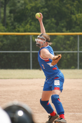 Softball pitcher delivering ball wearing face shield
