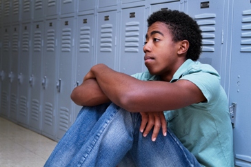 Sad African-American boy in front of school locker